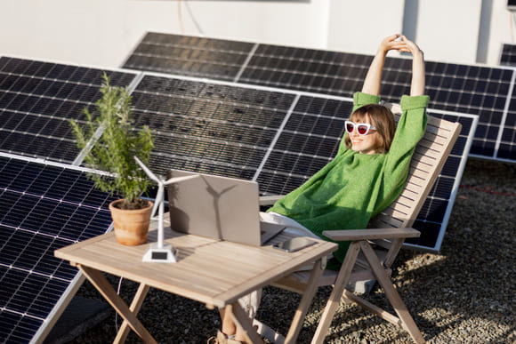 mujer estirando brazos delante del portátil con placas solares a su espalda