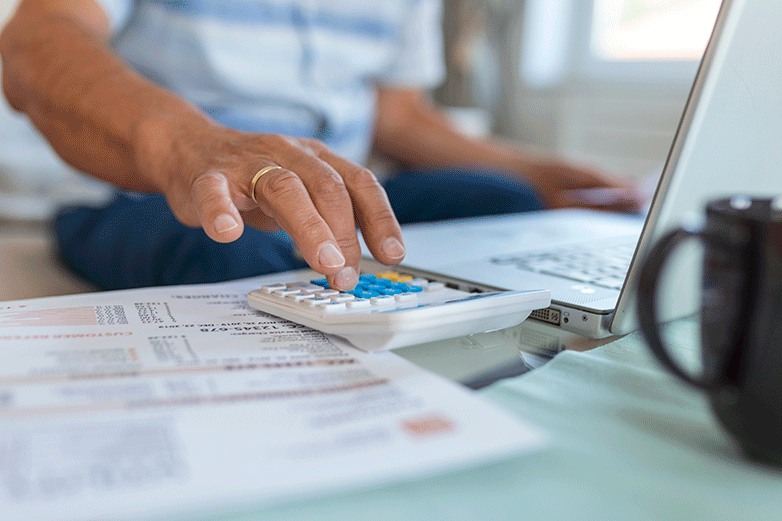 Hombre haciendo cálculos con sus facturas, calculadora y ordenador