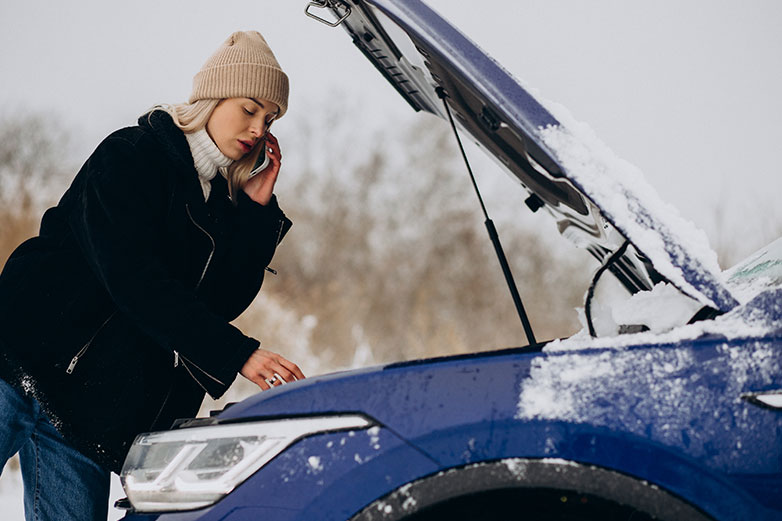Mujer al teléfono, revisando la batería del coche en invierno