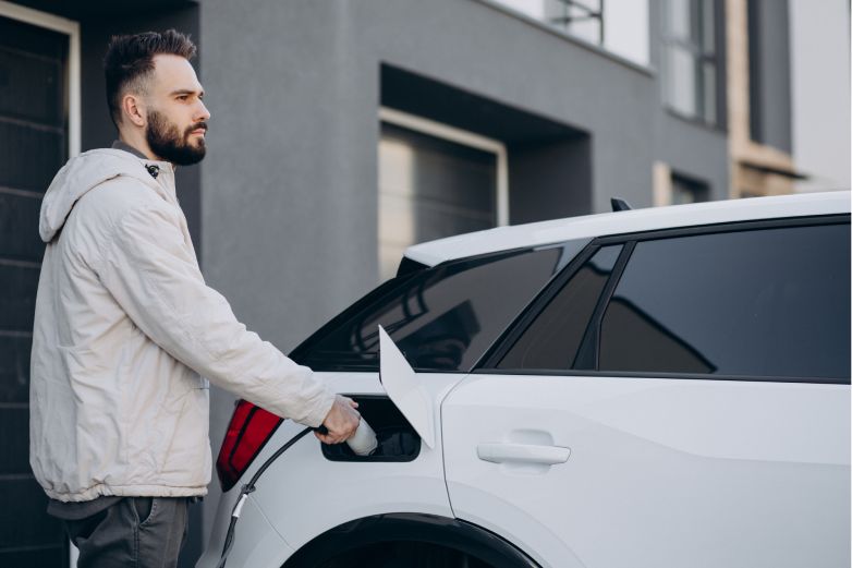 Hombre cargando el coche con el cargador eléctrico frente a su casa