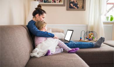 Mujer con su hija en el sofá viendo el portátil cerca del radiador