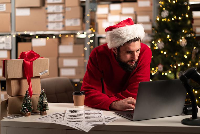Hombre con gorro de Navidad mirando el ordenador en el almacén