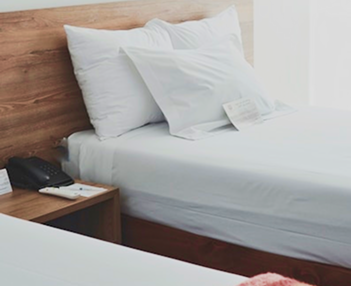 cama de hotel con s&aacute;banas y cojines blancos