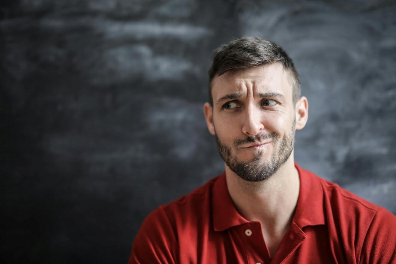 hombre joven con polo rojo con expresi&oacute;n pensativa pero a la vez alegre en el rostro.