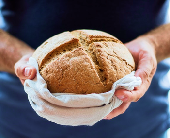 unas manos sostienen un pan redondo en una funda de tela blanca