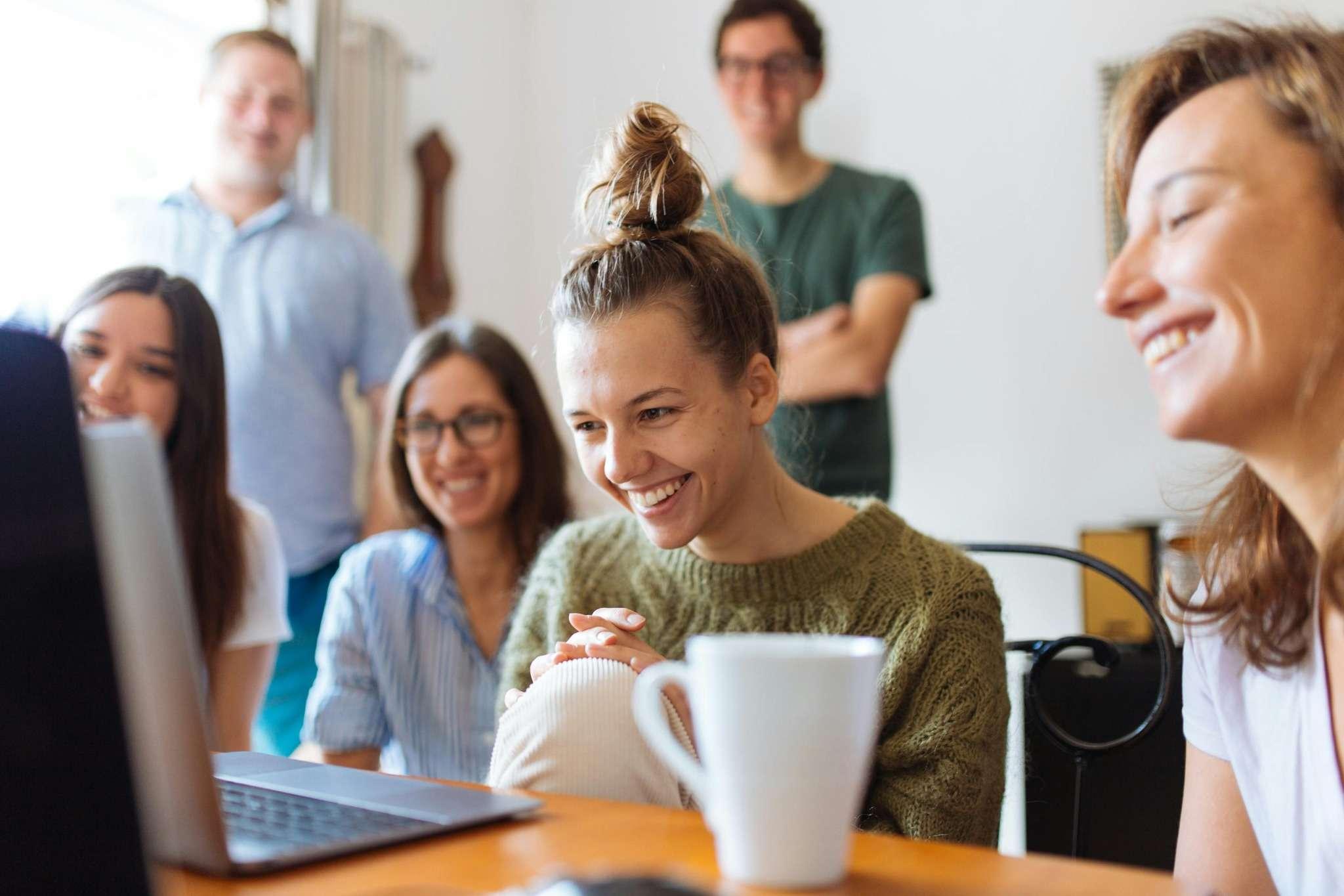 grupo de personas mirando la pantalla de un ordenador port&aacute;til con una amplia sonrisa en sus rostros.