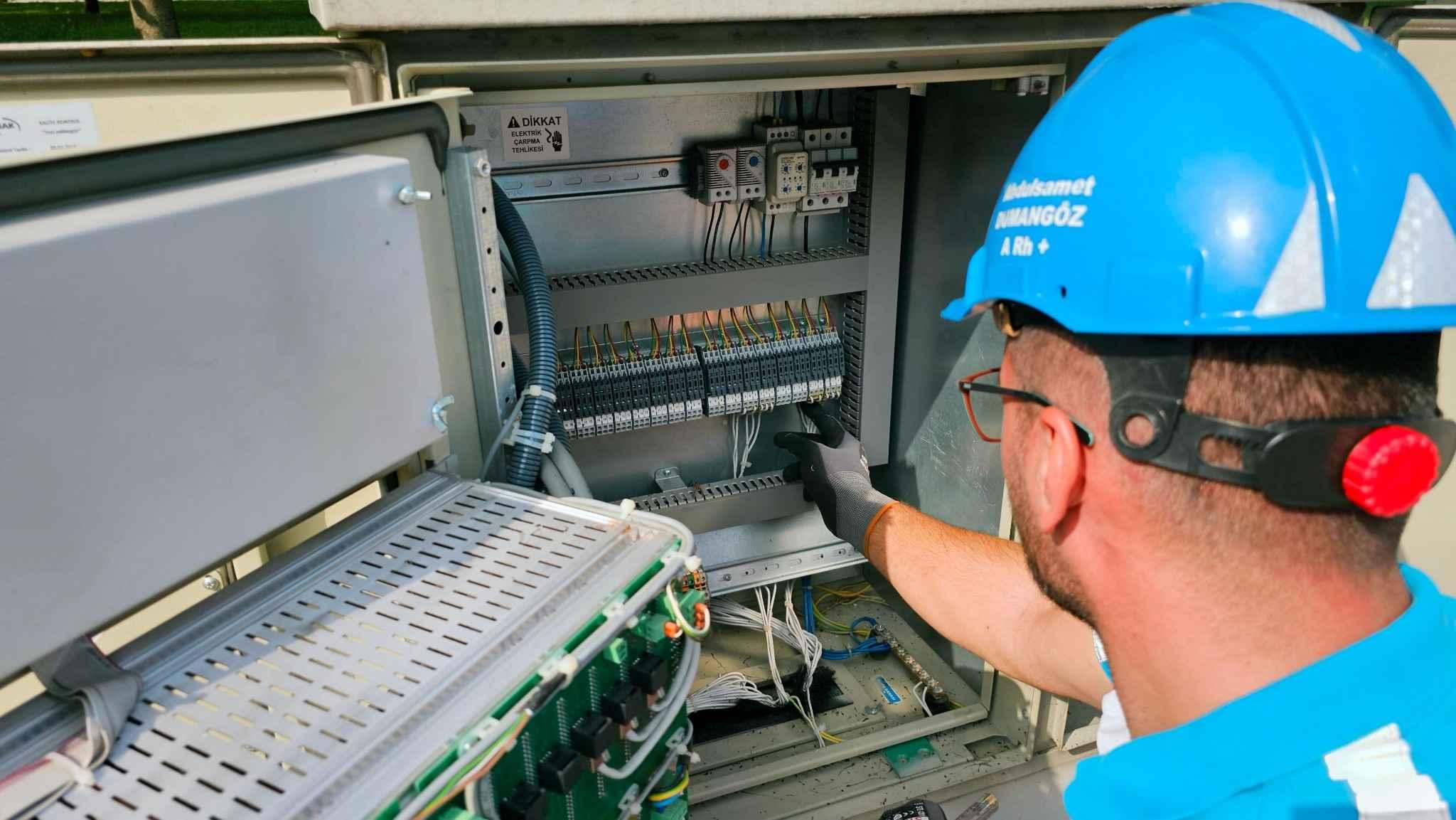 t&eacute;cnico vestido con un uniforme y un casco de protecci&oacute;n azul manipulando un contador de luz.
