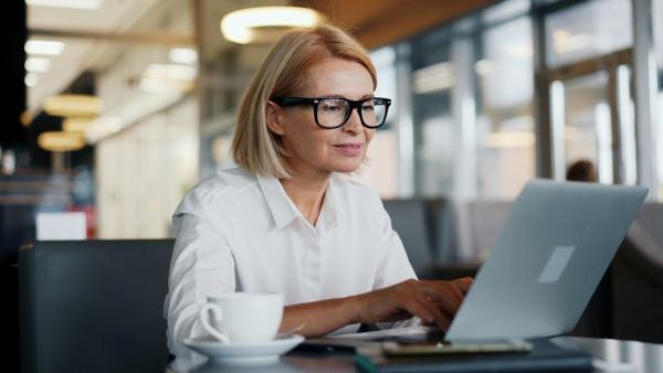 mujer escribiendo en su ordenador port&aacute;til con una expresi&oacute;n alegre y de tranquilidad en el rostro.
